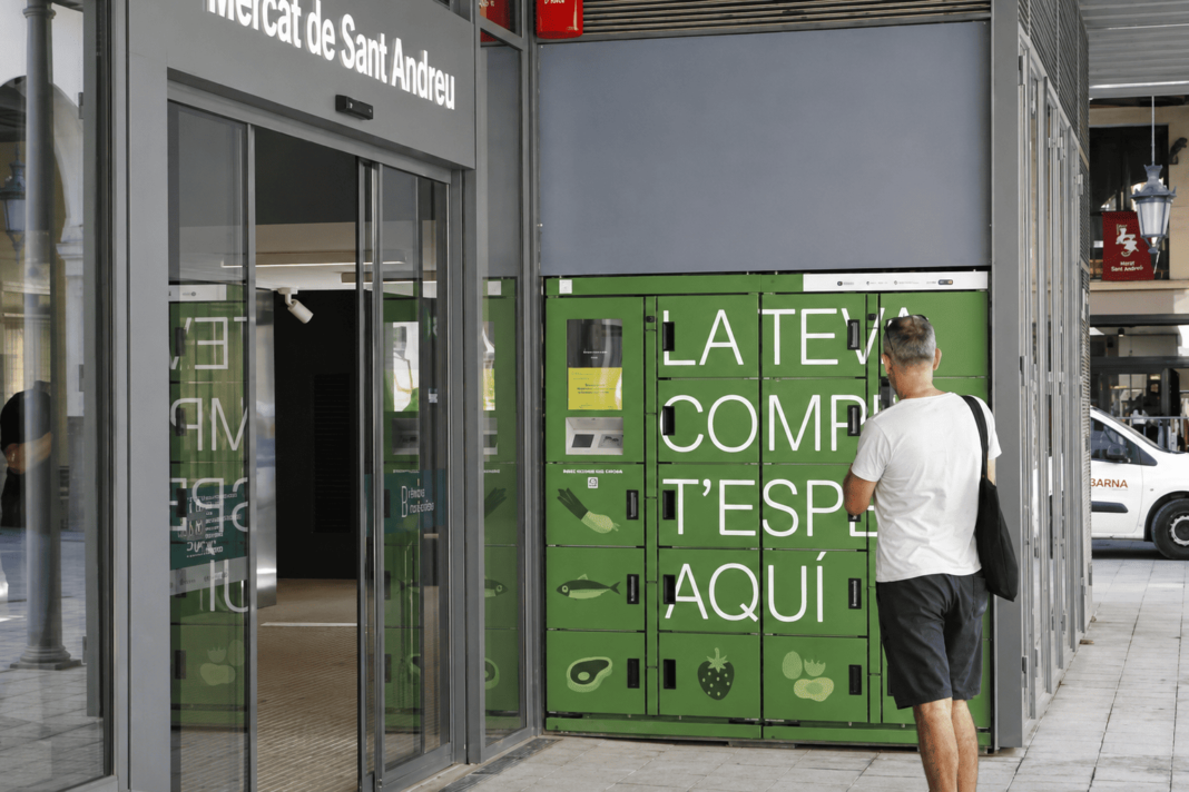 Una persona consulta les taquilles de recollida de compres a l’entrada del Mercat de Sant Andreu.