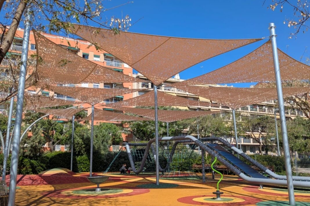 Àrea de joc infantil amb estructures tèxtils d’ombra instal·lades sobre els elements de joc.