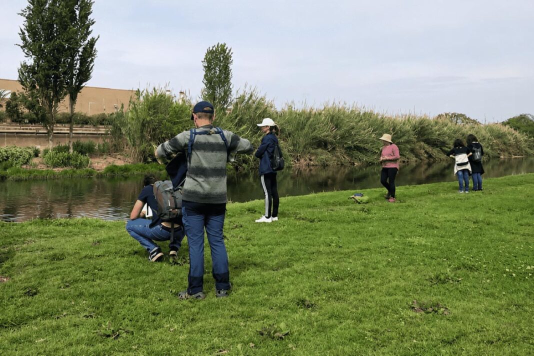 Grup de persones observant l’entorn natural en una zona verda al costat del riu Besòs.