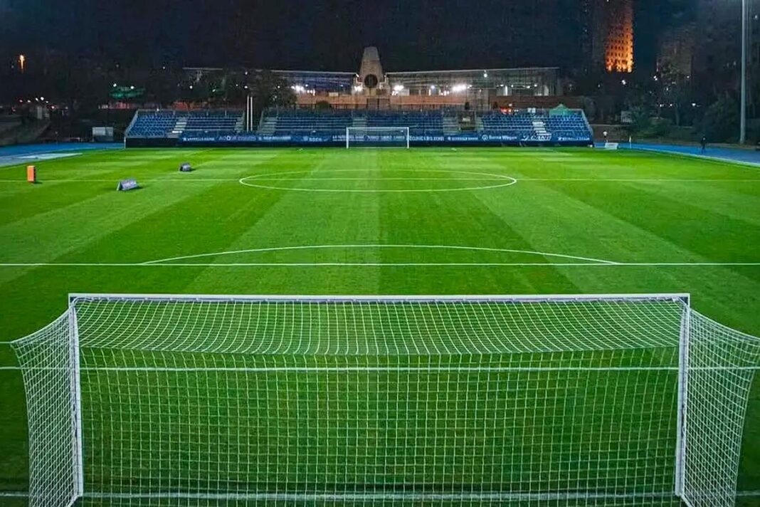 Camp de futbol de Can Dragó il·luminat de nit, vist des de darrere d’una porteria