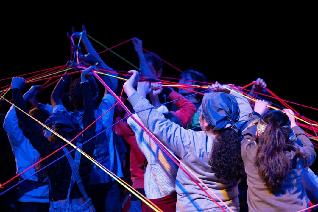 Participants de ‘Campamento galáctico, d’AzconaToloza, sostenen i entrecreuen cordes de colors durant l’espectacle de teatre participatiu.