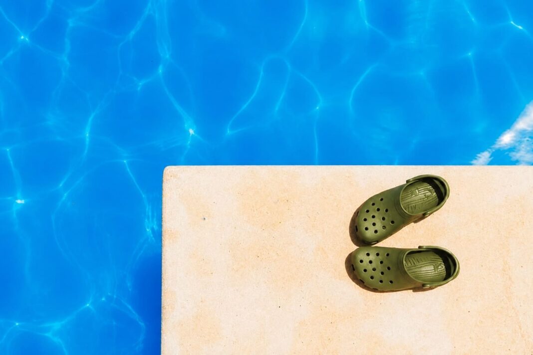 Un parell de sabots verds al marge d’una piscina amb l’aigua blava