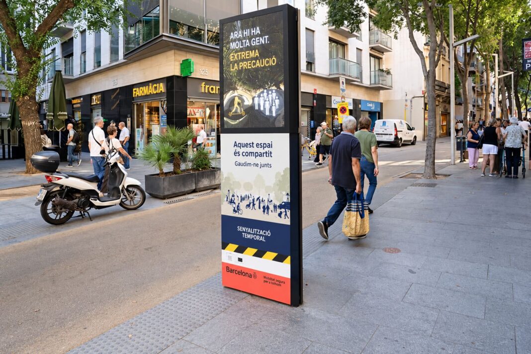 Tòtem informatiu de la prova pilot REALLOCATE al carrer Gran de Sant Andreu amb vianants i vehicles compartint l’espai públic